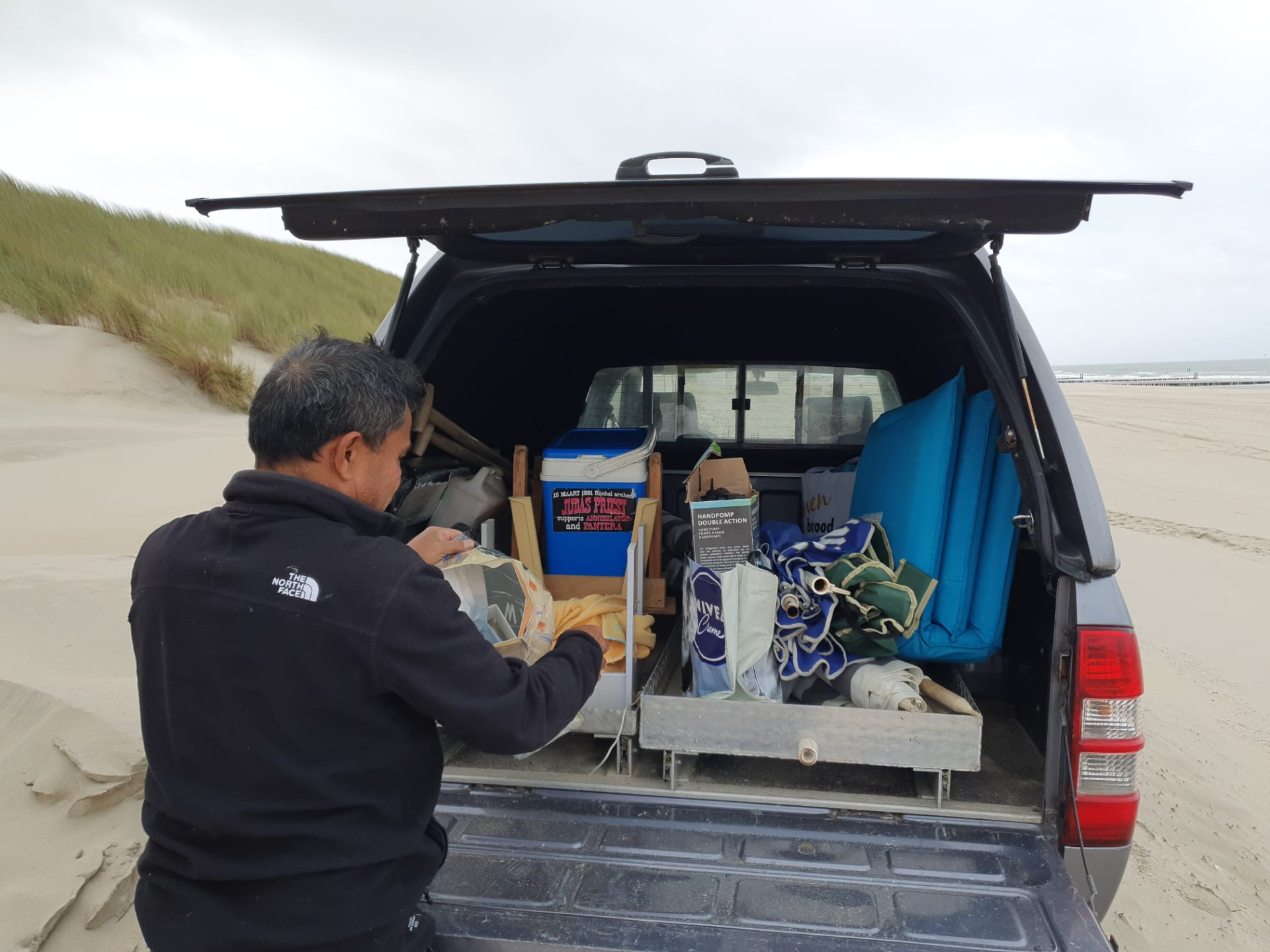 Nakman laadt strandspullen in de auto op het strand van Walcheren